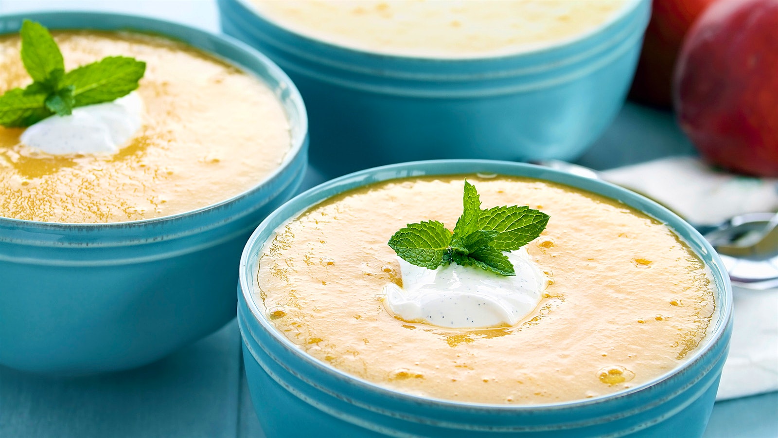 Bowls of chilled peach soup topped with a dollop of cream and mint leaves